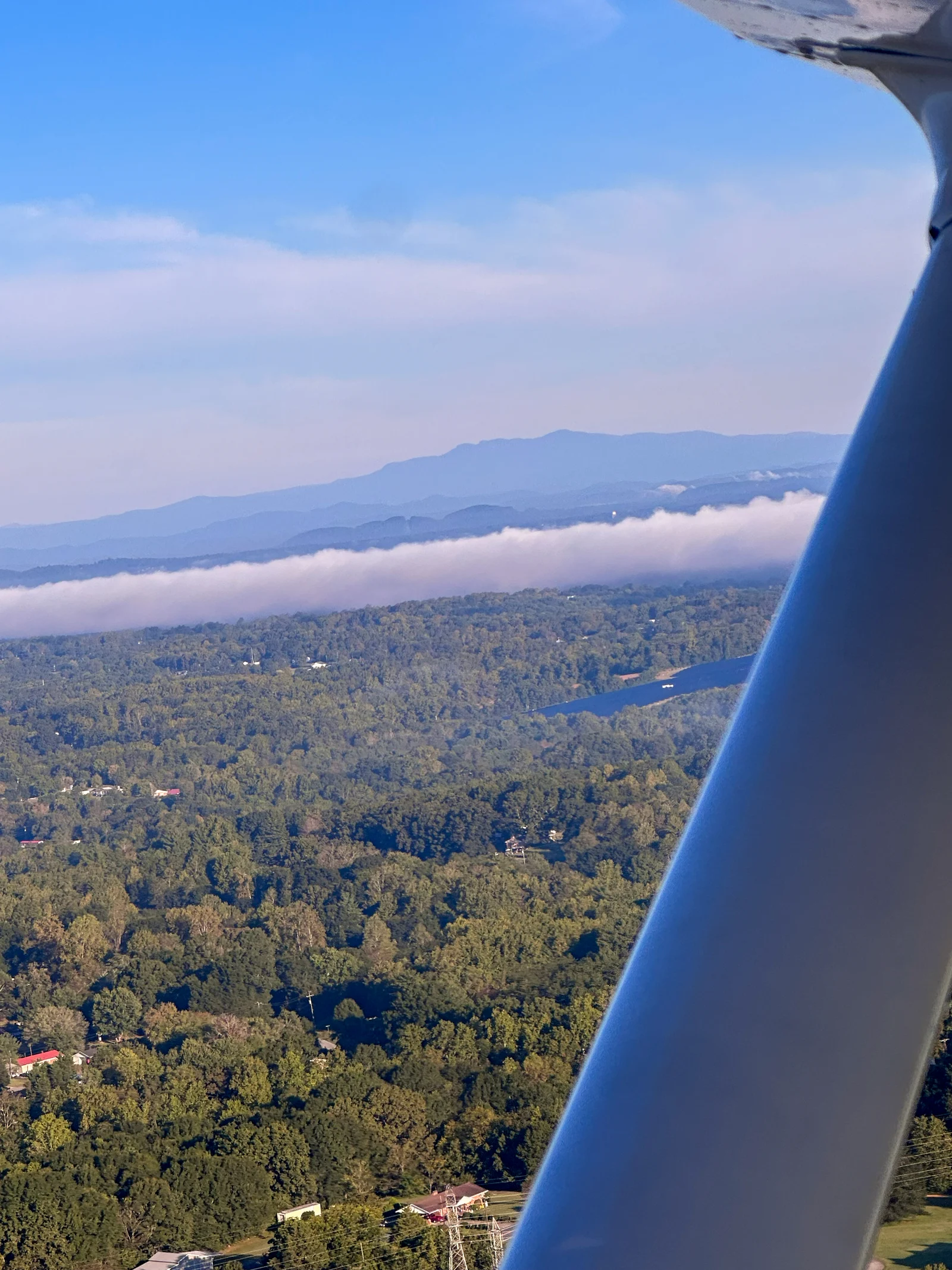 View beside an aircraft wing strut toward wooded terrain and distant mountains